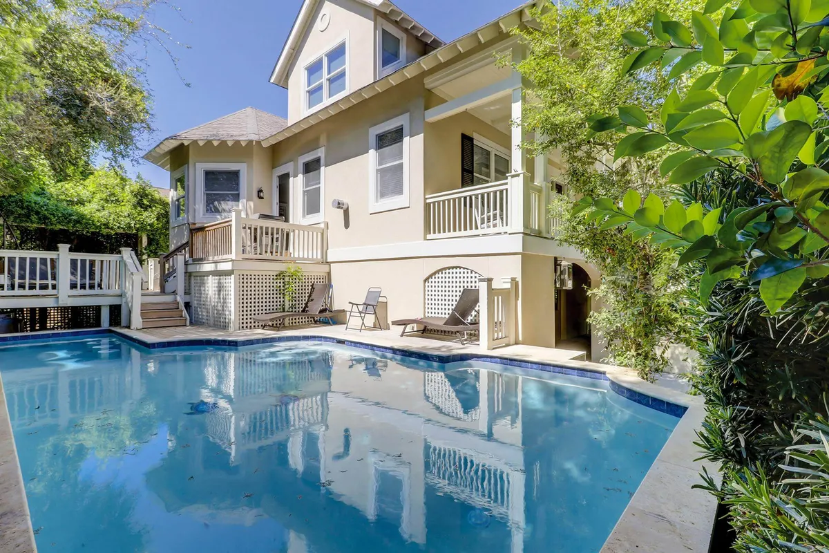 The exterior view showcases a sparkling swimming pool surrounded by a spacious deck area, bordered by lush greenery and the home's exterior. Sun loungers and outdoor seating create a relaxed, family-friendly atmosphere for sunbathing, swimming, or dining al fresco.