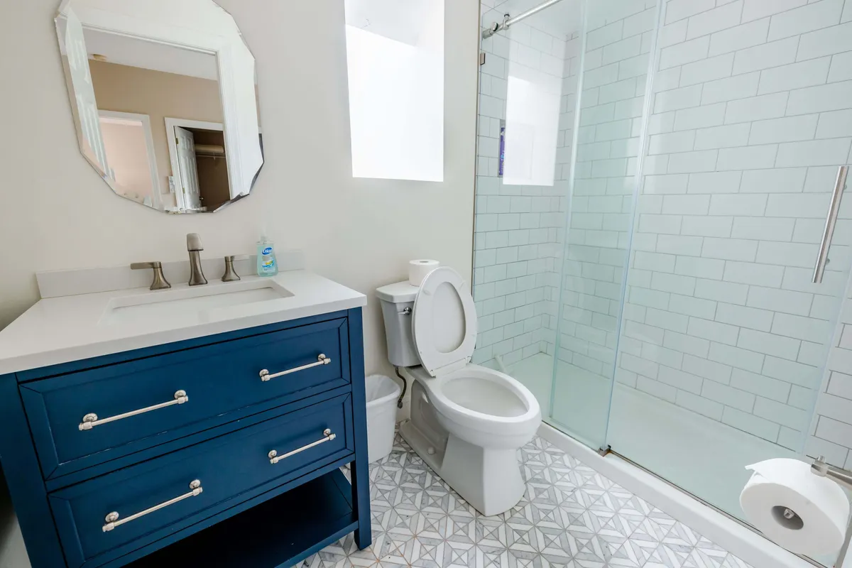 A fresh and inviting ensuite bathroom featuring a blue vanity, a large mirror reflecting natural light, and a glass shower enclosure. The clean lines and soothing palette offer a sense of relaxation and private self-care.