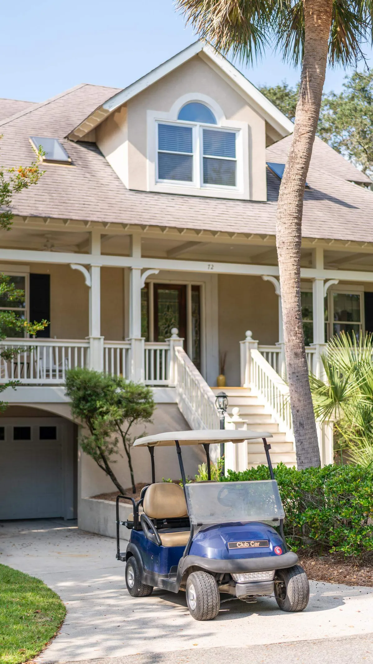 The hero image showcases the front of a charming Hilton Head Island single-family home, surrounded by lush landscaping. A welcoming front porch invites guests to relax, while a stylish golf cart sits ready for neighborhood adventures. The mood is leisurely, evoking a vacation vibe perfect for families or groups eager to explore and unwind.