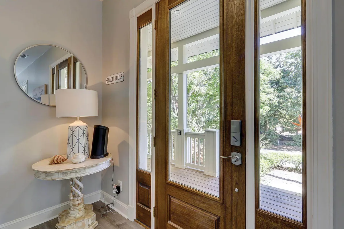 This image shows a set of double doors leading to the outdoors, a round mirror, a table lamp, and a decorative entry table. Sunlight appears to filter in, and the scene conveys a welcoming transition from inside to outside, hinting at the possibilities for exploration beyond the home.