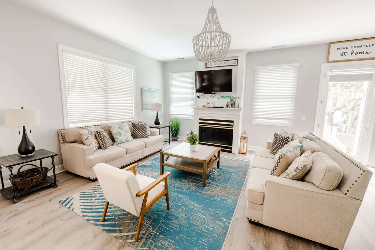 A cozy living room scene featuring plush sofas, a central coffee table, a glowing fireplace, and a classic chandelier overhead. The atmosphere is comfortable and social, designed for relaxing, reading, or enjoying a game night with loved ones.