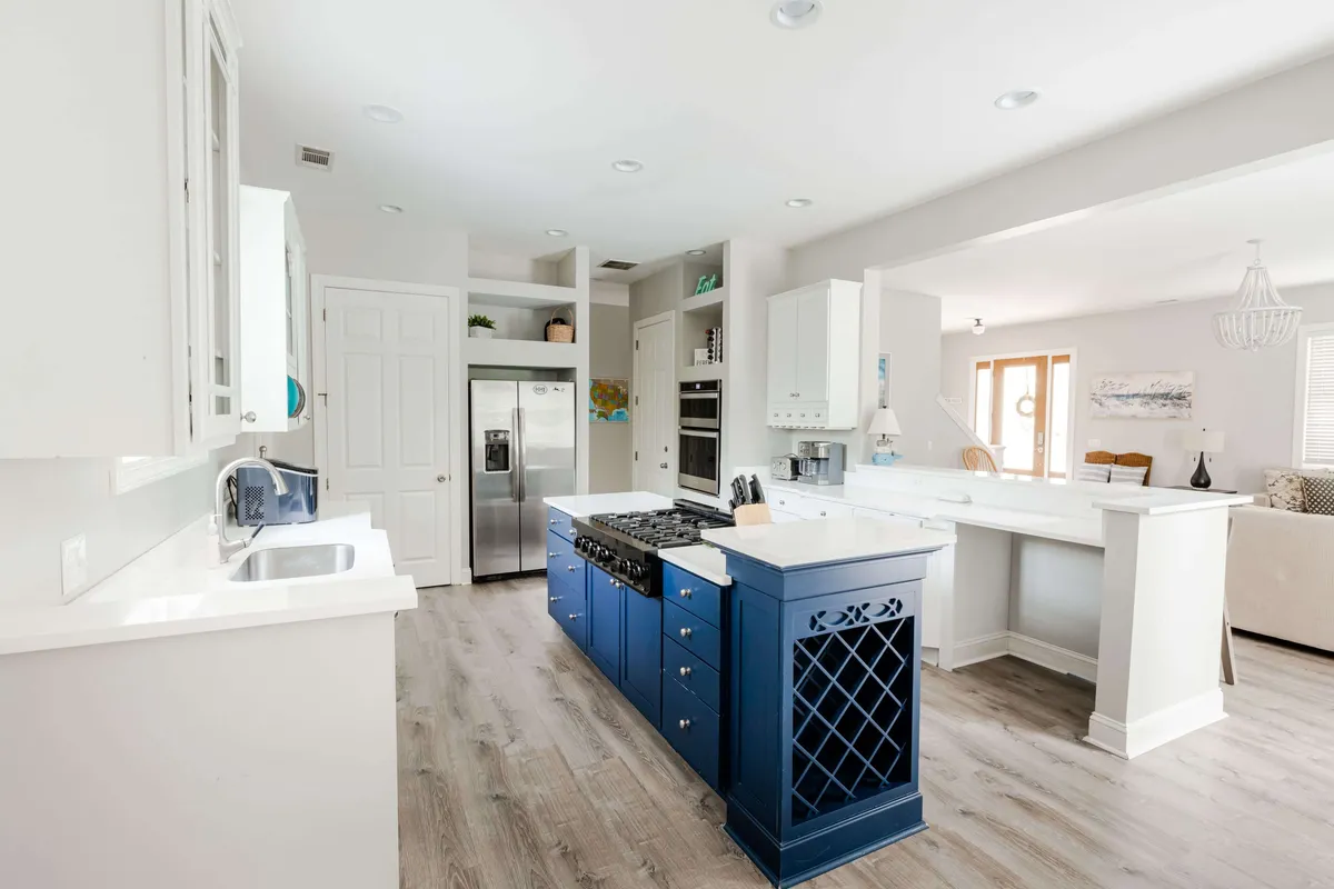 A modern kitchen with a striking blue island, stainless steel appliances, and an open layout. Natural light pours in through windows, illuminating the space and highlighting the kitchen's role as a hub for both casual and festive meals. The setting suggests a seamless flow for entertaining, baking, and sharing stories across seasons.